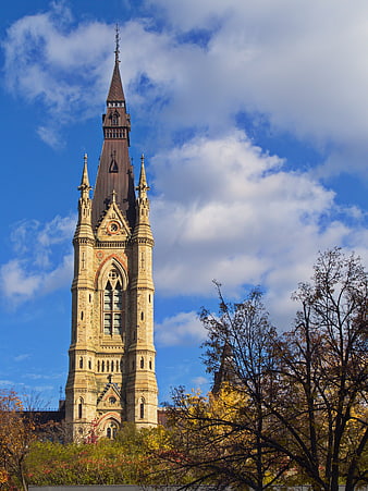 Gothic church tower with spire against blue sky and autumn trees