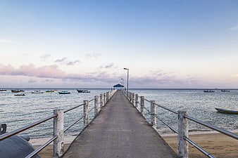 Concrete pier extending into calm ocean with boats at sunset