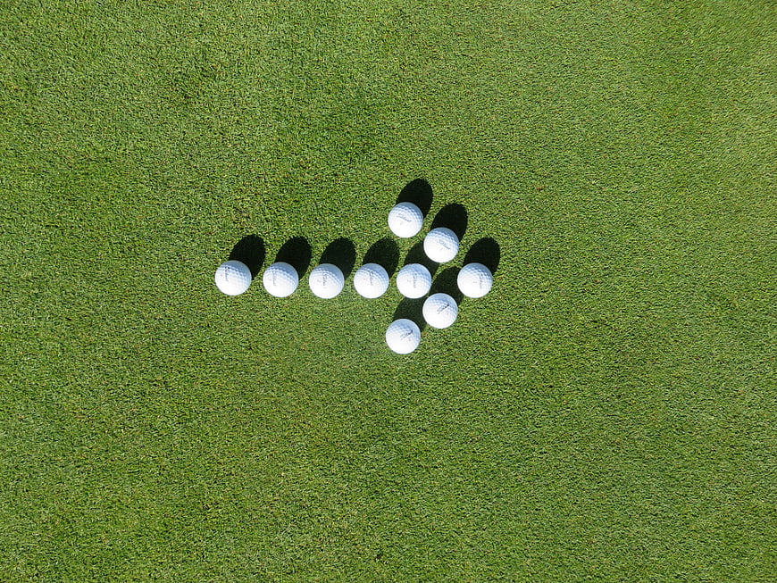 Golf Balls Arranged In Arrow Shape On Green Grass