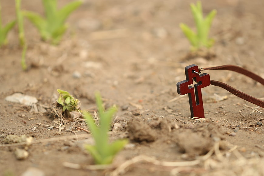 Wooden Cross Necklace in Garden Soil with Sprouts