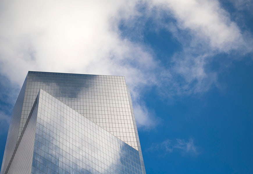 Modern glass skyscraper reflecting clouds against blue sky