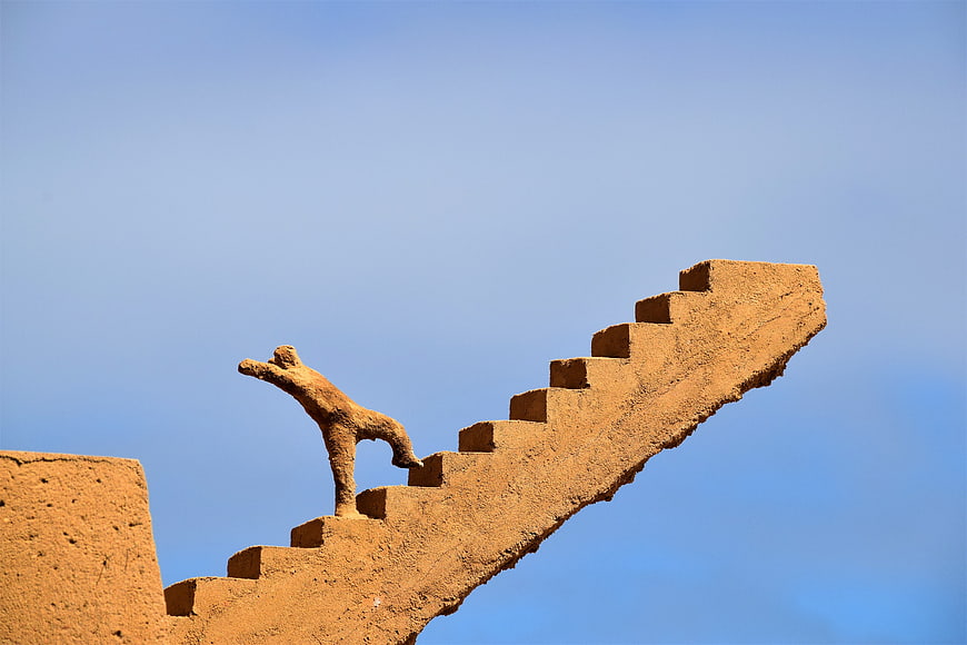 Sand sculpture of a figure climbing stairs against a blue sky