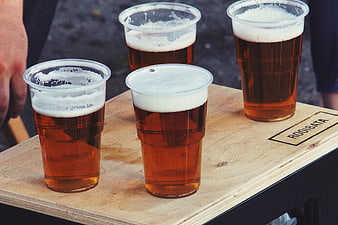 Four plastic cups of amber beer with foam on a wooden table