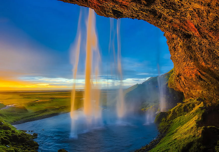 View from behind a waterfall at sunset with cave opening