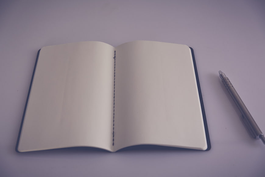 Open blank notebook with pen on purple background