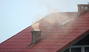 Smoke rising from brick chimney on red tiled roof