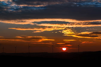 Silhouette of wind turbines against a dramatic sunset sky