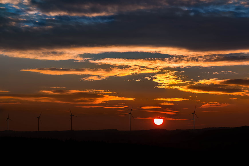 Silhouette of wind turbines against a dramatic sunset sky