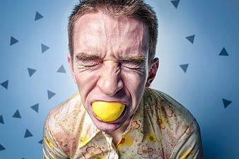 Man making sour face while biting a whole lemon