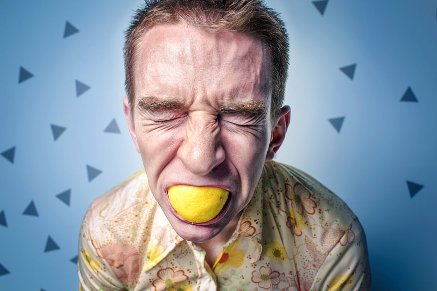 Man making sour face while biting a whole lemon