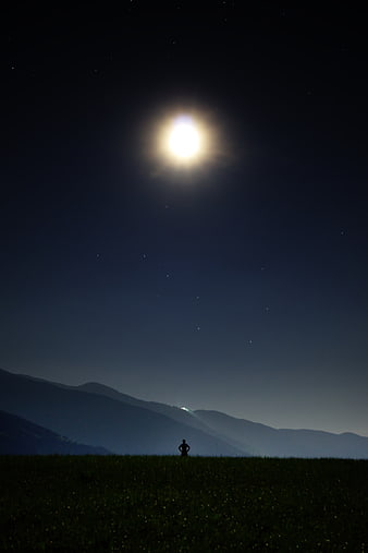 Silhouette of Person Standing in Field Under Bright Moon and Stars