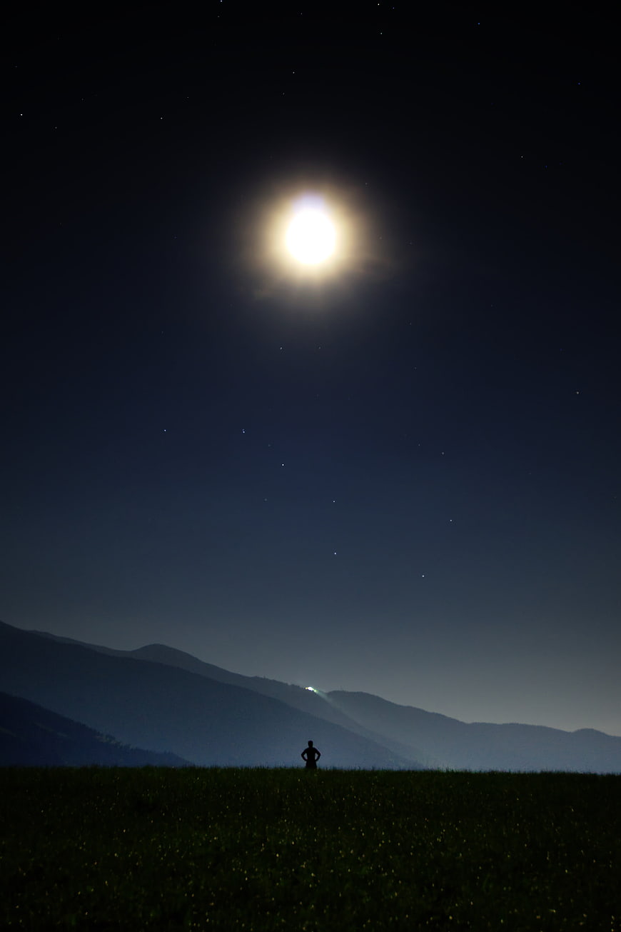 Silhouette of Person Standing in Field Under Bright Moon and Stars