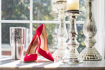 Red heels and coffee tumbler on windowsill with candlesticks