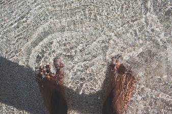 Bare feet in clear shallow water on pebbly beach