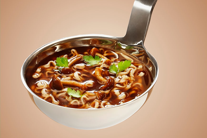 Metal Ladle with Dark Noodle Soup and Parsley Garnish