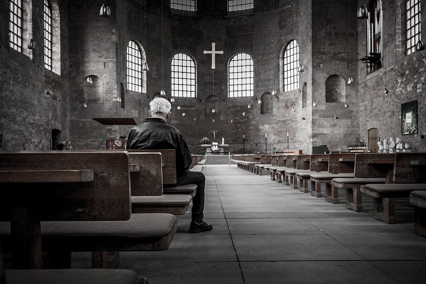 Senior man praying alone in rustic stone church interior