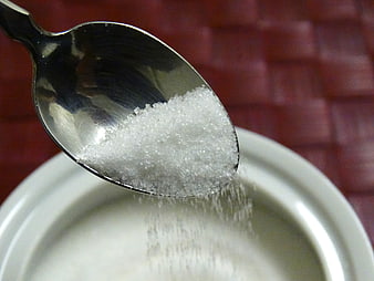 Close-up of white sugar pouring from a metal spoon into a bowl