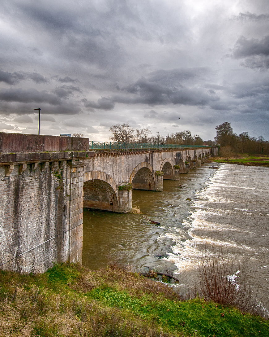 Historic stone arch bridge over flowing river under cloudy sky