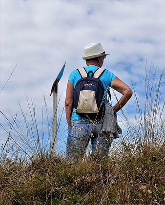 Senior woman hiking with backpack on grassy hill