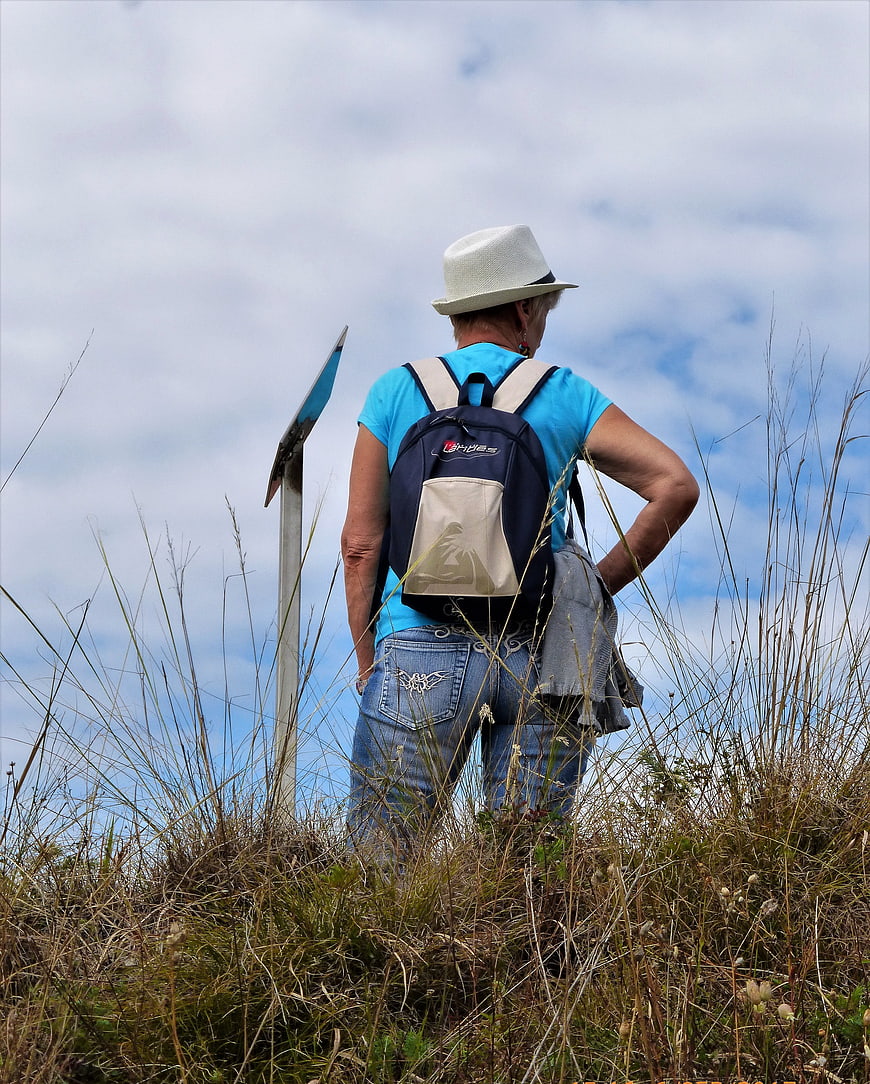 Senior woman hiking with backpack on grassy hill