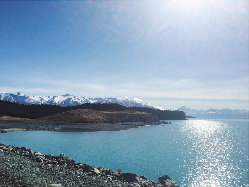 Scenic turquoise lake with snow-capped mountains and rocky shore