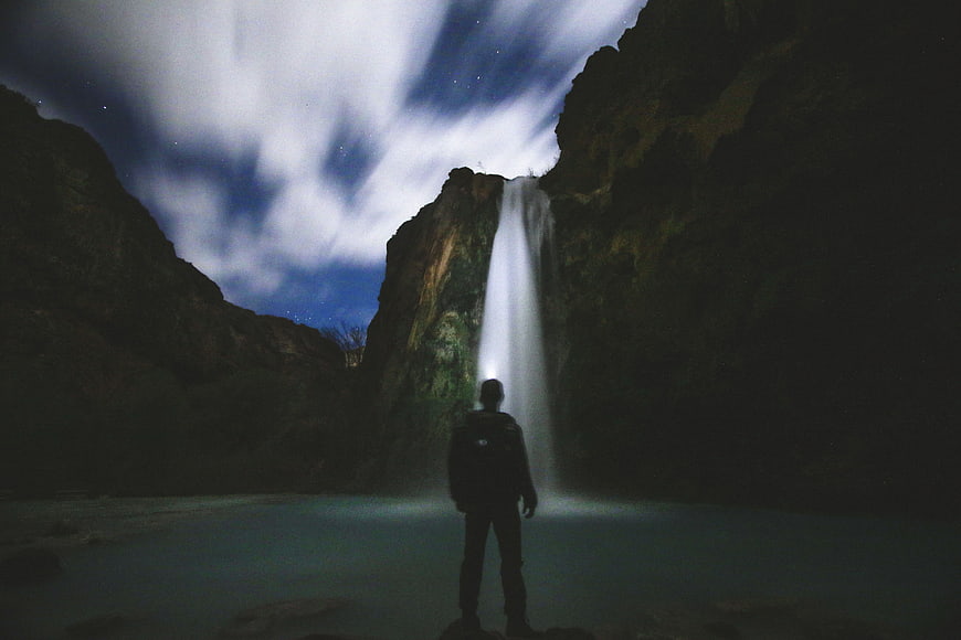 Silhouette of Man Standing Before Waterfall at Night