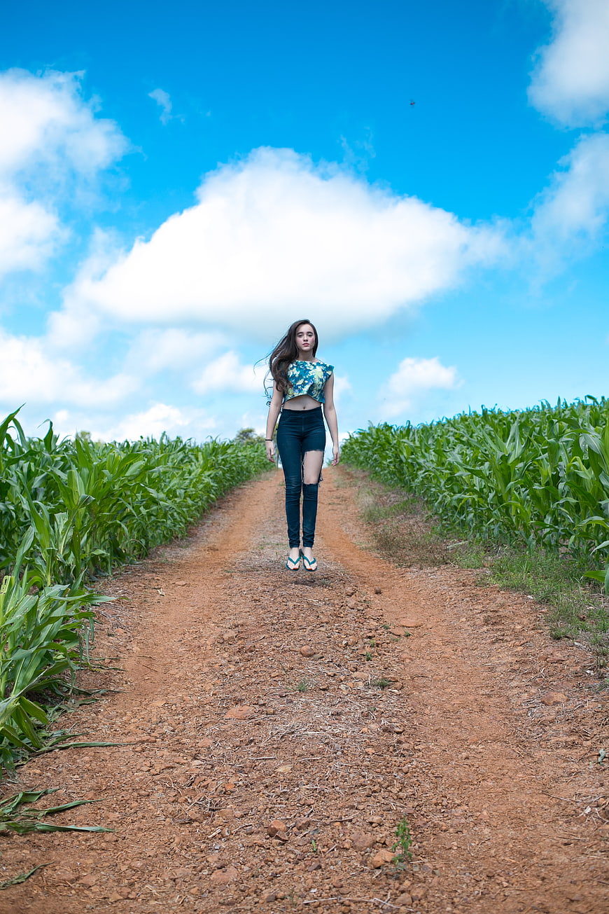 Young Woman Jumping on Dirt Road in Cornfield