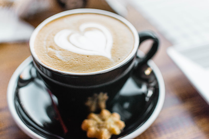 Heart Latte Art in Black Cup with Cookie on Wooden Table