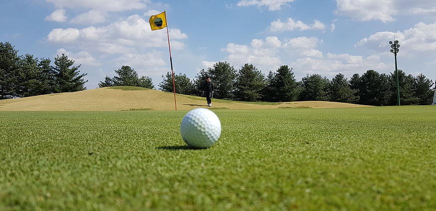 Golf ball on green with flag and golfer in background