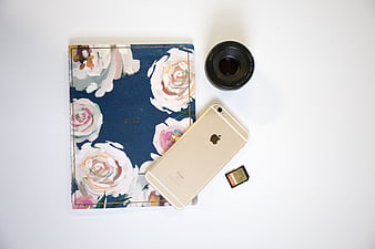 Flat lay of floral planner, smartphone, and camera lens on white background