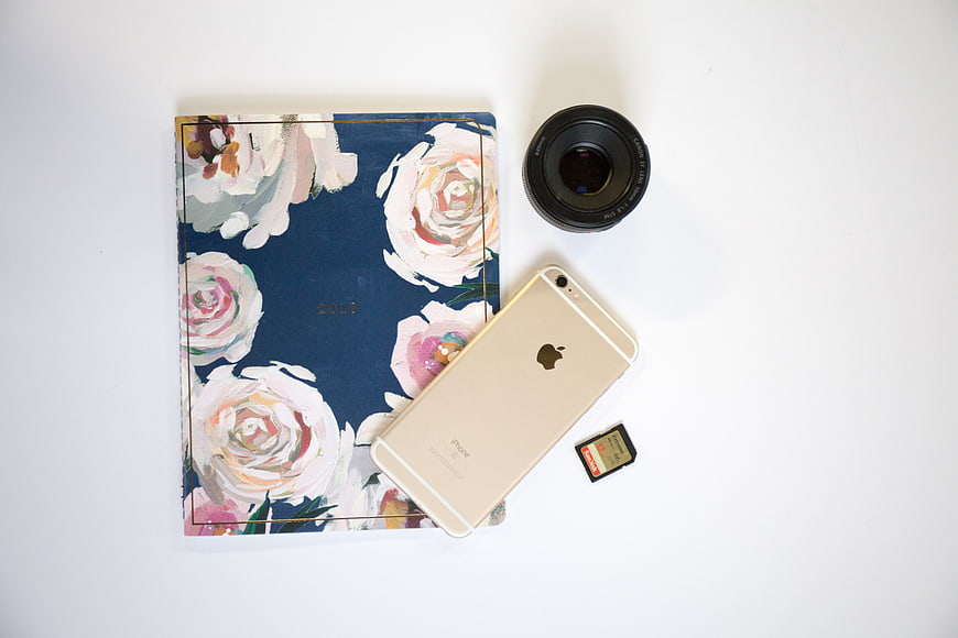 Flat lay of floral planner, smartphone, and camera lens on white background