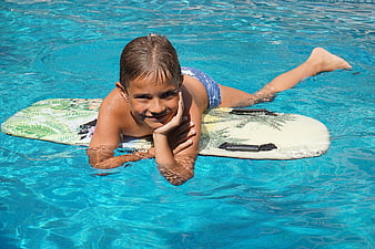 Happy boy lying on surfboard in swimming pool