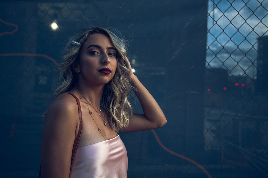 Stylish Blonde Woman in Pink Top Against Urban Fence