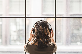 Woman with headphones listening to music by rainy window