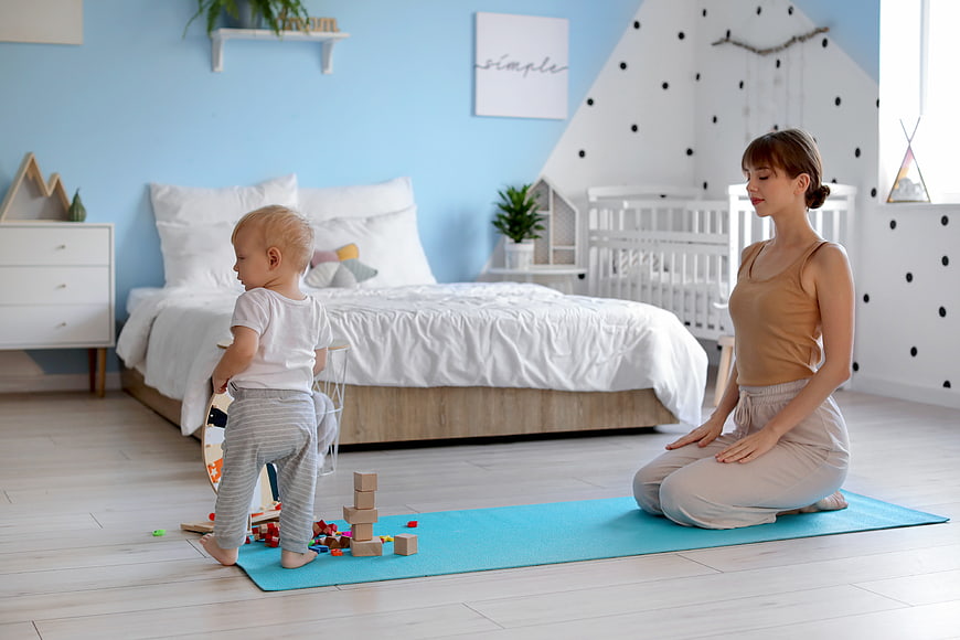 Mother meditating while toddler plays with blocks in bedroom