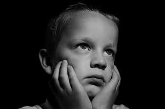Black and white portrait of a young boy looking up with hands on face