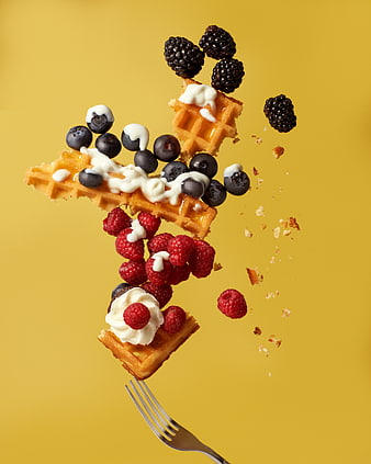 Waffle pieces with berries and cream flying off a fork