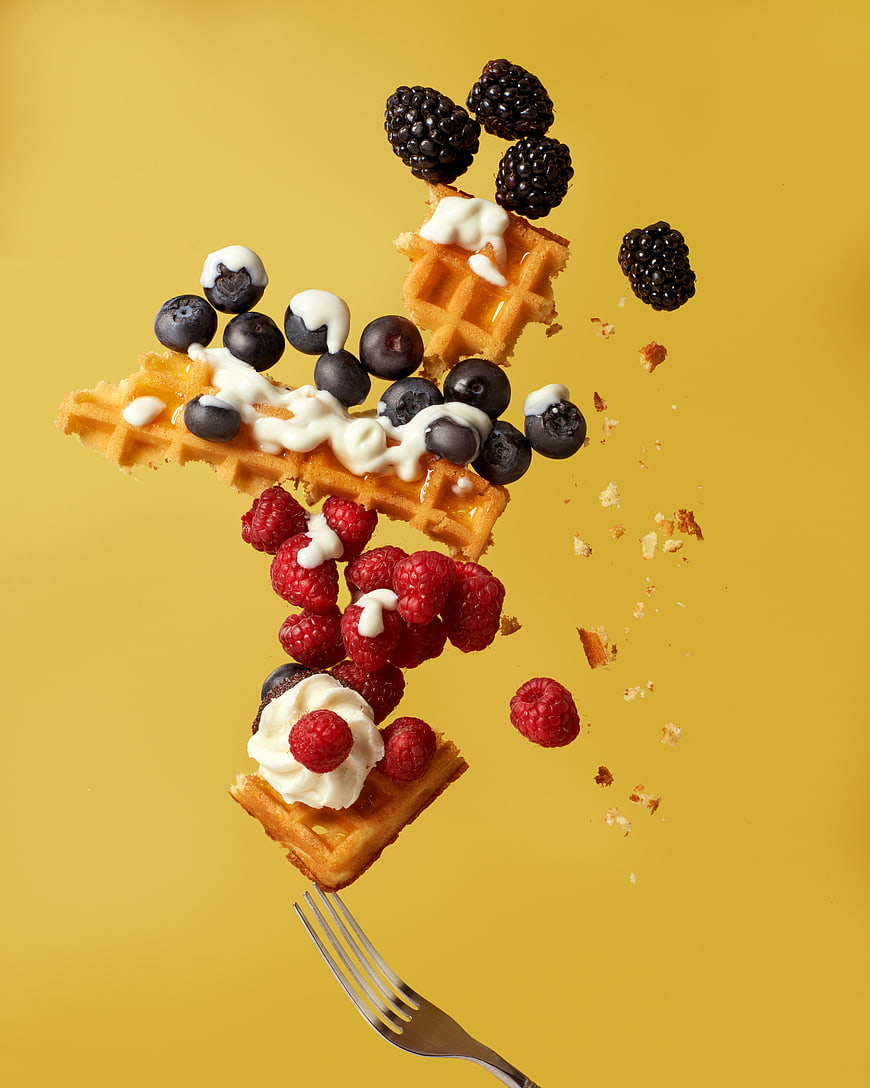 Waffle pieces with berries and cream flying off a fork