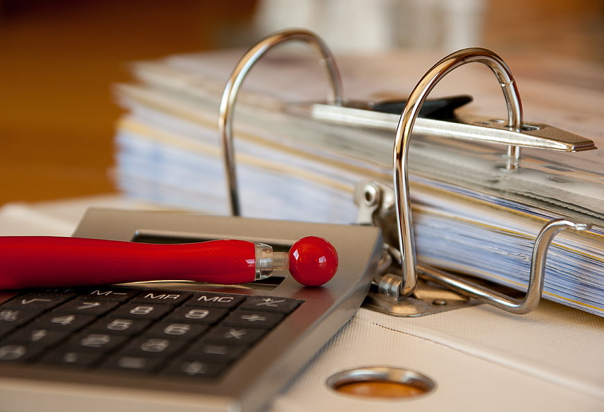 Close-up of calculator, red pen, and ring binder on desk