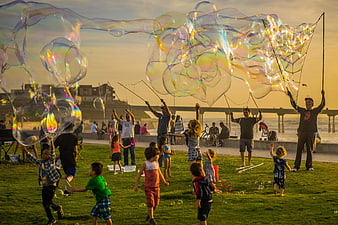 Giant iridescent bubbles floating over children playing on a beach at sunset