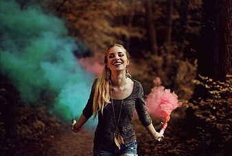 Joyful Woman Holding Colorful Smoke Bombs in Autumn Forest