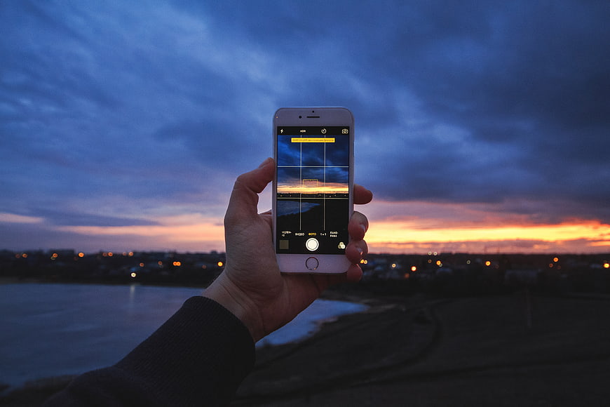 Hand holding smartphone capturing sunset over city skyline