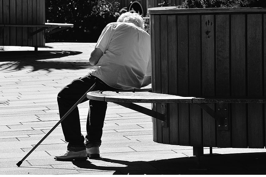 Senior man sitting alone on park bench with cane