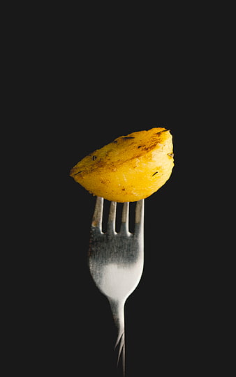 Roasted potato wedge on a fork against a black background