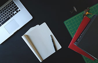 Flat lay of laptop, notebook, pen, and books on dark desk