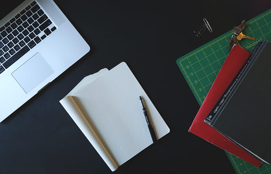 Flat lay of laptop, notebook, pen, and books on dark desk