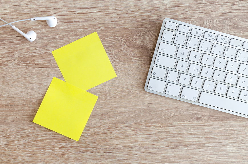 Flat lay of workspace with keyboard, sticky notes, and earphones
