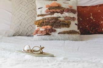 Reading glasses on book with textured pillows on bed