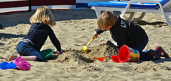 Two Children Playing With Sand Toys On A Sunny Beach
