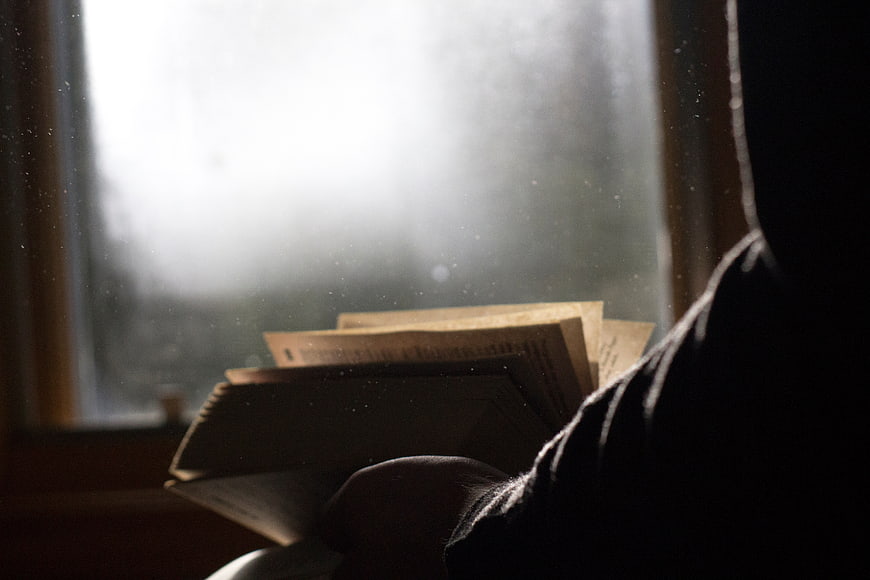 Person Reading Book by Window in Rainy Atmosphere